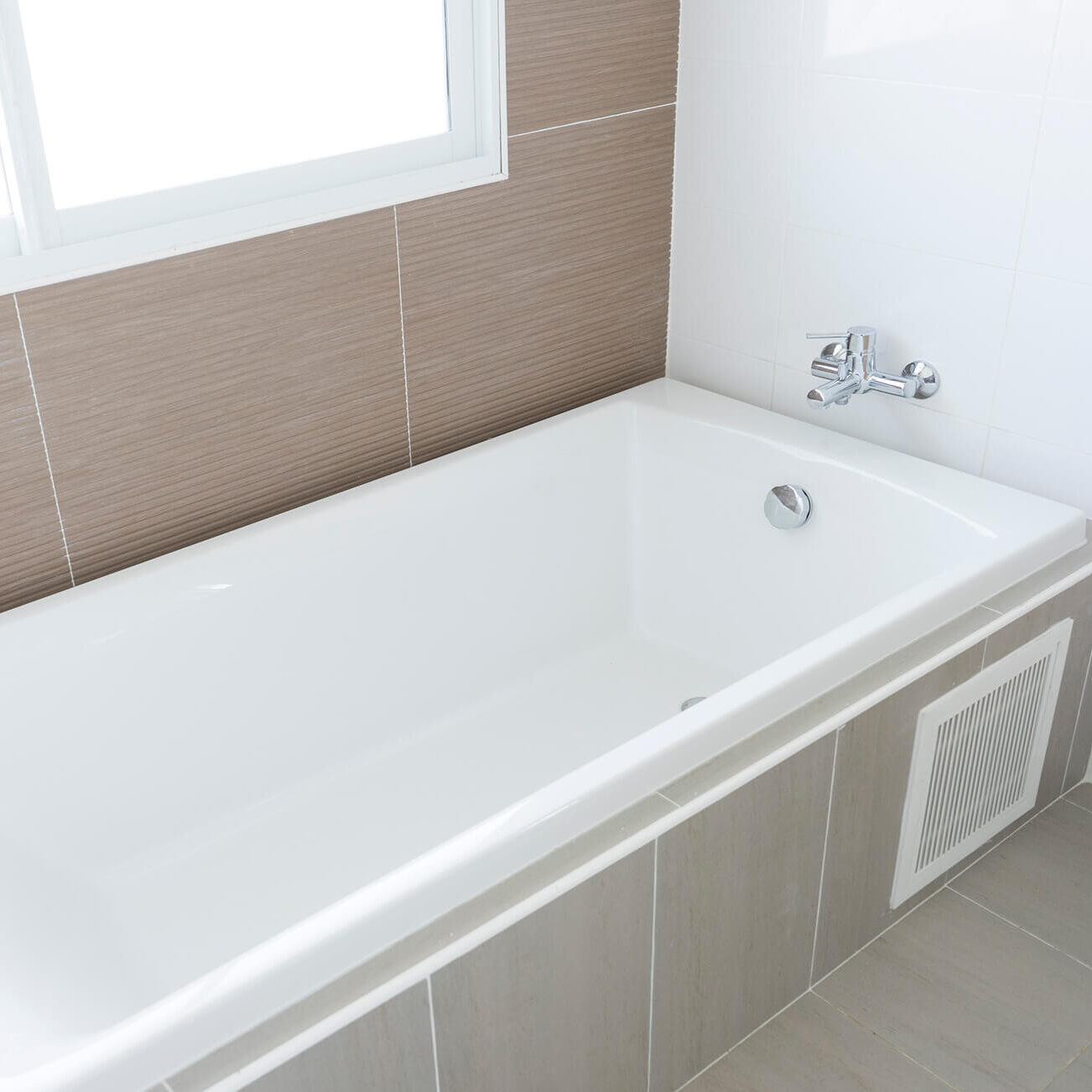 White bathtub with modern faucet and tiles.